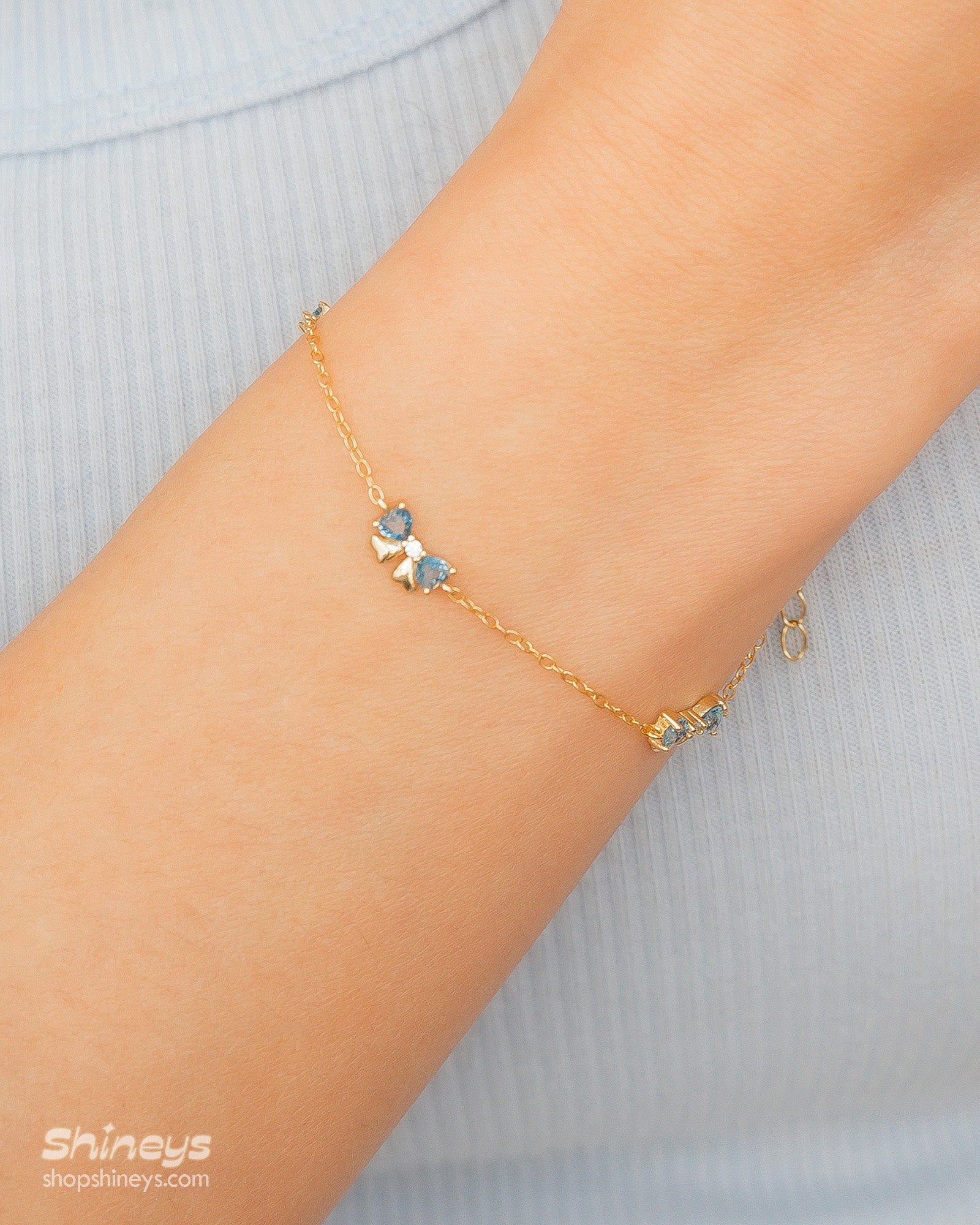 A dainty gold-toned bracelet with three tiny bows crafted from sparkling blue heart-cut zircons