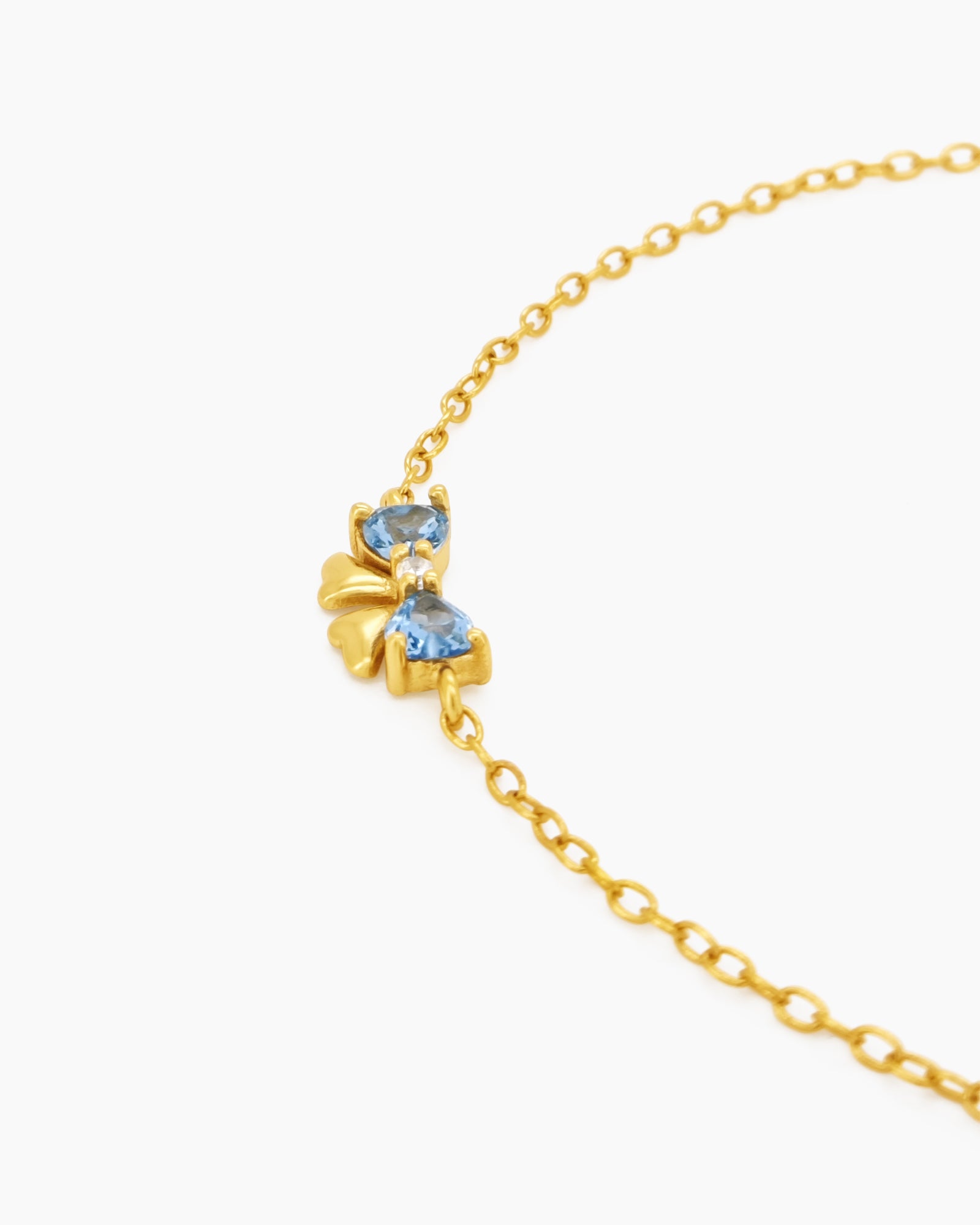 A dainty gold-toned bracelet with three tiny bows crafted from sparkling blue heart-cut zircons