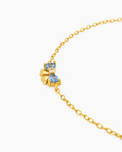 A dainty gold-toned bracelet with three tiny bows crafted from sparkling blue heart-cut zircons