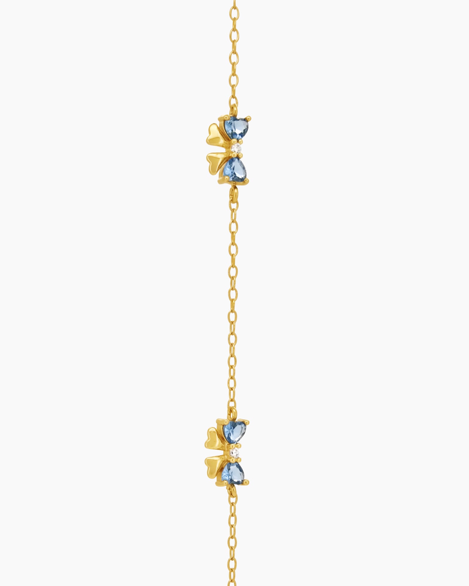 A dainty gold-toned bracelet with three tiny bows crafted from sparkling blue heart-cut zircons