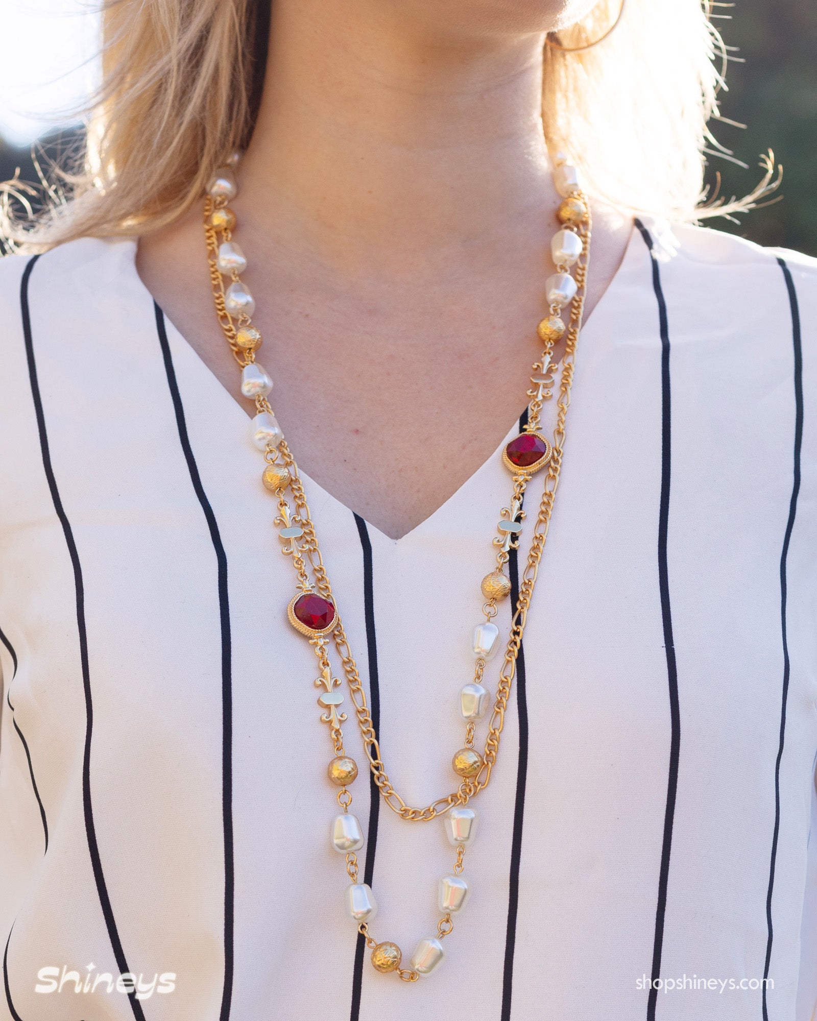 An opera-length necklace with ornate gold links, soft faux pearls, and deep red glass stones