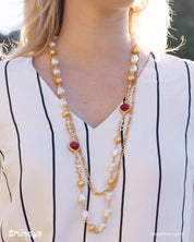 An opera-length necklace with ornate gold links, soft faux pearls, and deep red glass stones