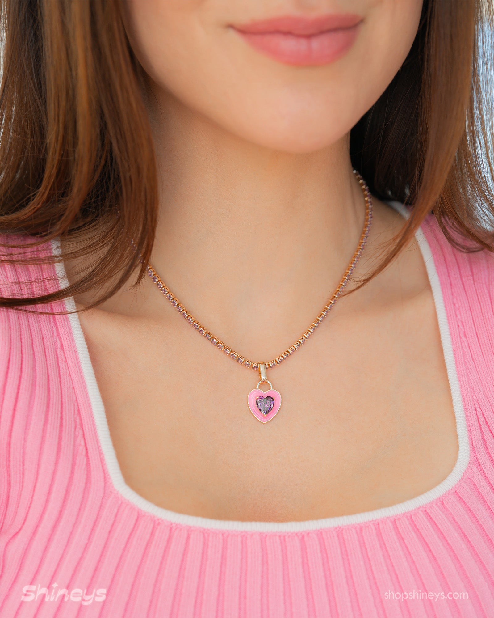 A light-pink tennis necklace with a full strand of zircon stones and an enamel heart charm with a center stone