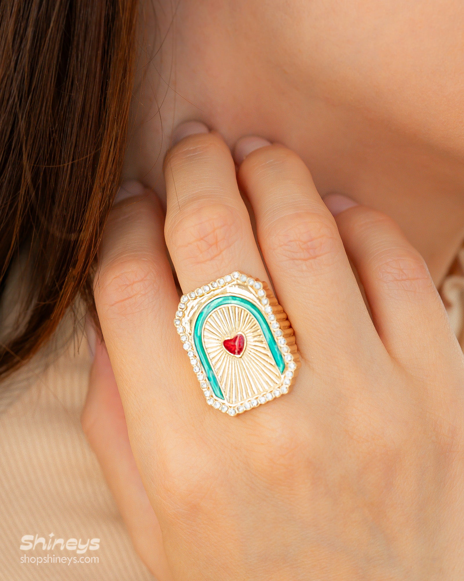 A golden statement ring with a ridged, sculptural form and a zircon red heart in a dreamy arched frame
