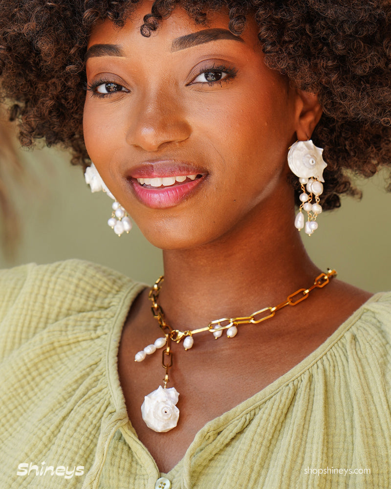 A chunky gold-tone paperclip chain necklace with delicate pearl droplets and a statement conch shell pendant