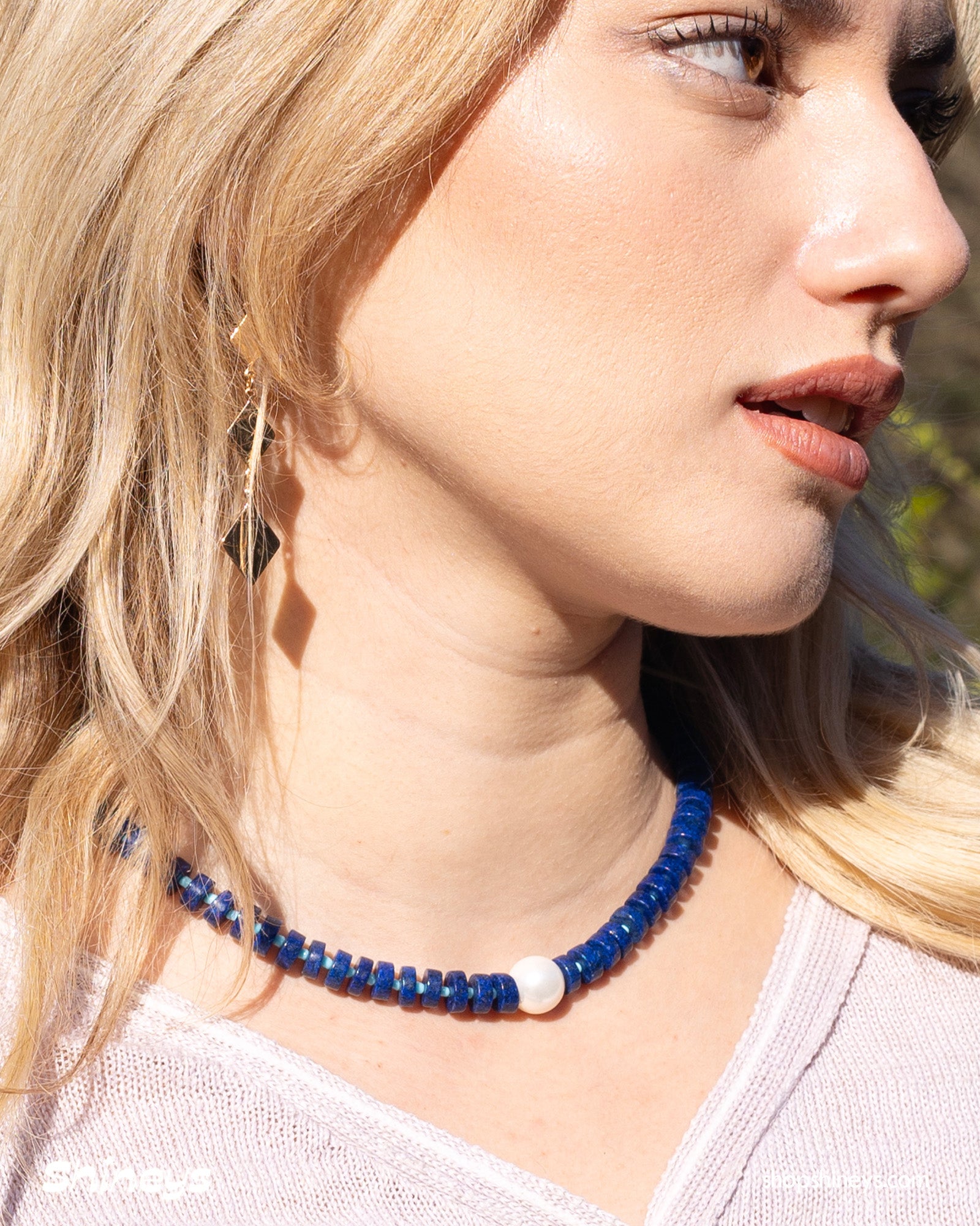 A sleek, structured necklace of navy-blue lapis lazuli beads with a glossy freshwater pearl at its heart