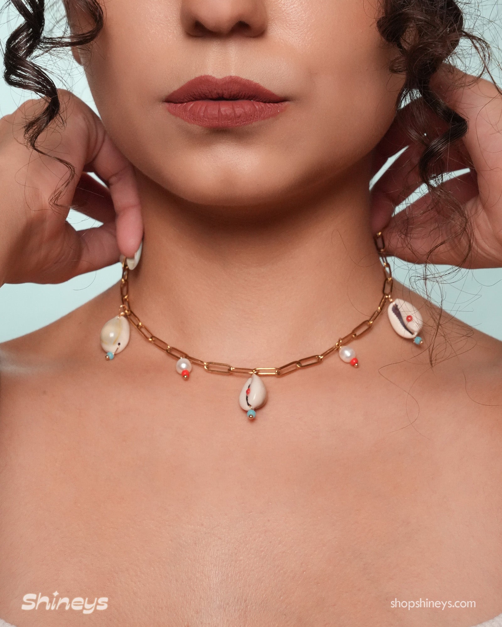 A necklace with cowrie shells, freshwater pearls, and beads on a bold gold link chain for a seaside flair