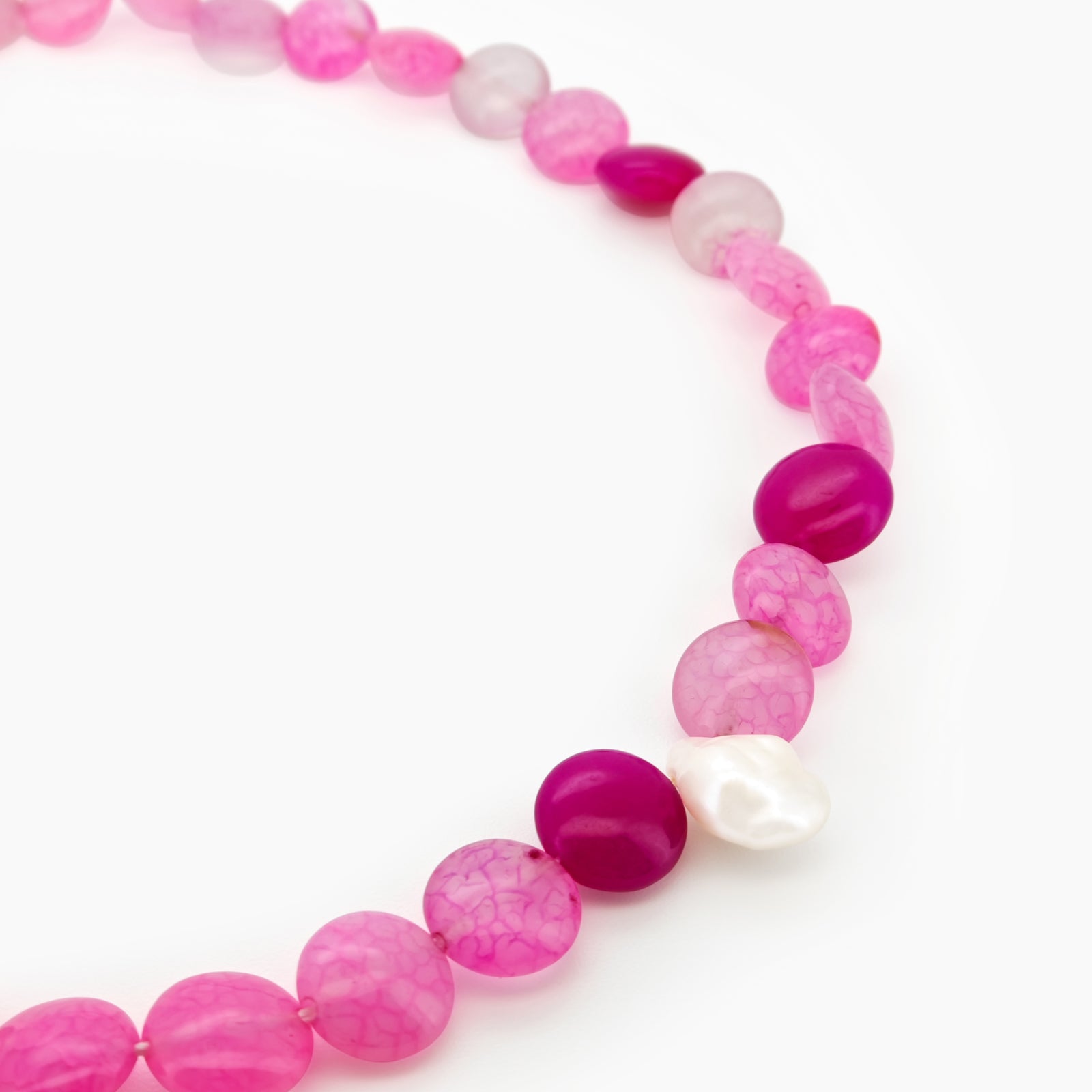 A beaded necklace with vibrant hot pink and translucent blush carnelian, accented by a single baroque pearl