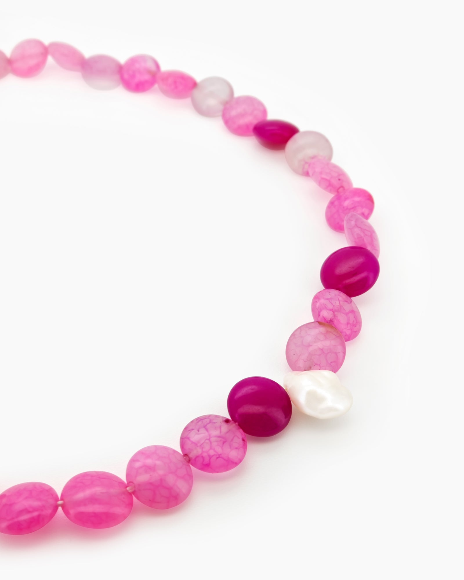 A beaded necklace with vibrant hot pink and translucent blush carnelian, accented by a single baroque pearl